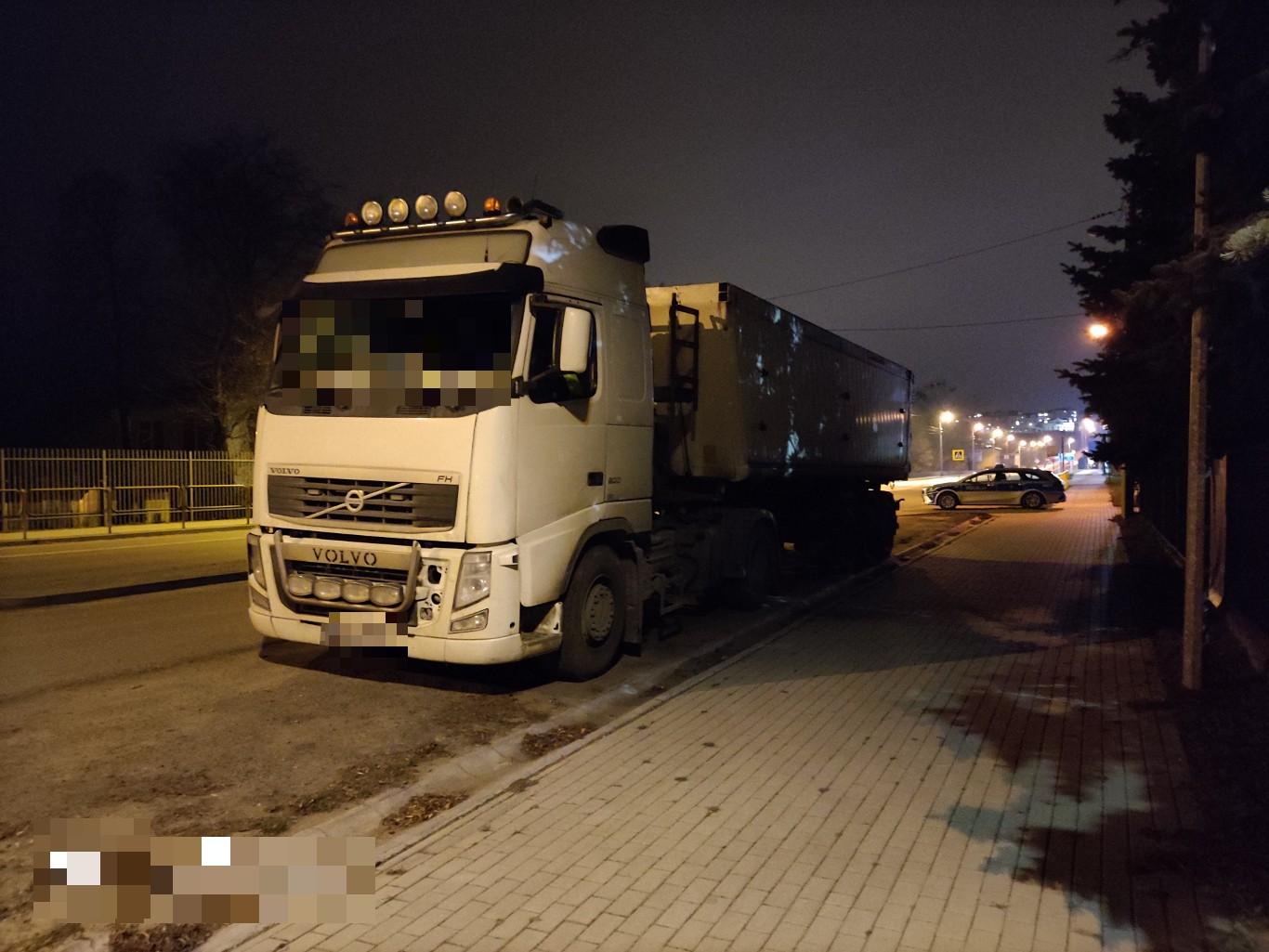 Punkt kontrolny przy drodze. Na pierwszym planie zestaw członowy: ciągnik samochodowy marki Volvo wraz naczepą. Z tyłu, radiowóz policyjny.