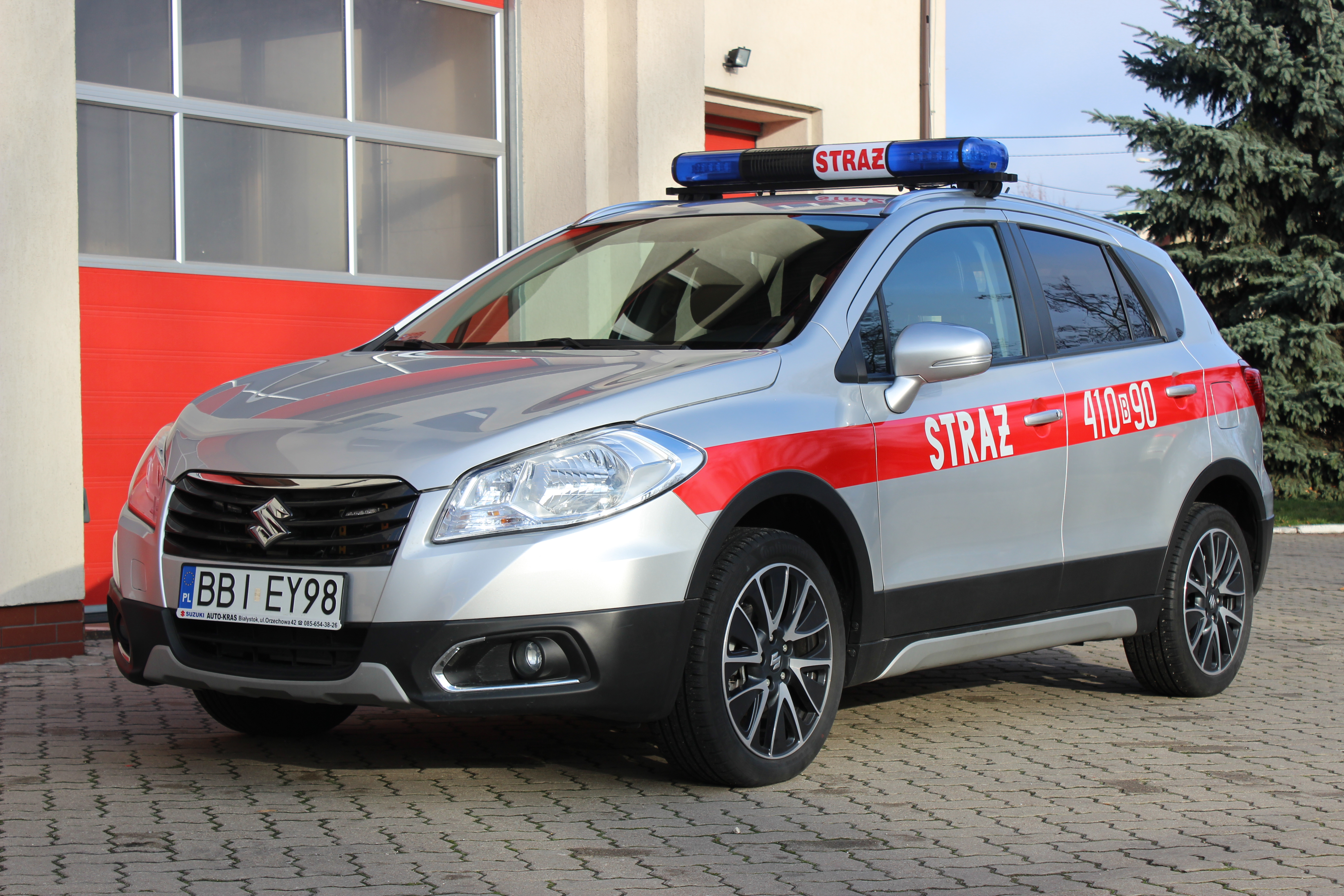 Zdjęcie przedstawia samochód operacyjny SUZUKI s-cross stojący na tle strażnicy.