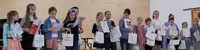 Grupa stojących dzieci. W rękach trzymają dyplomy i torebki z upominkami.