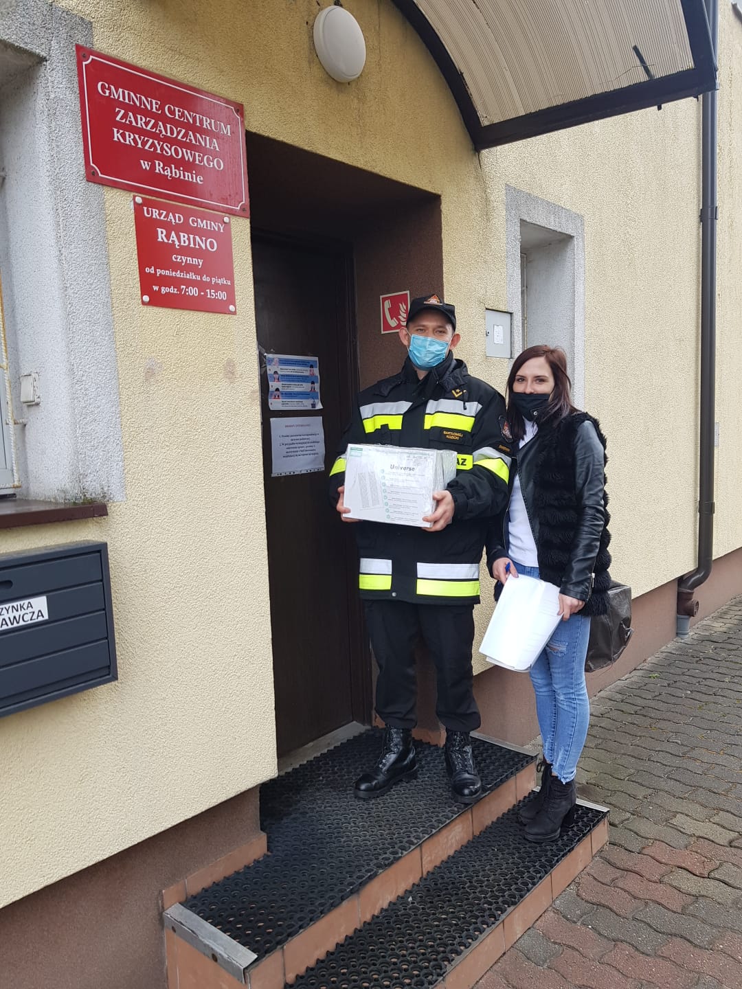 Zdjęcie przedstawia strażaka oraz młodą kobietę, którzy wchodzą do siedziby gminy Rąbino z kartonem ulotek #szepimysię