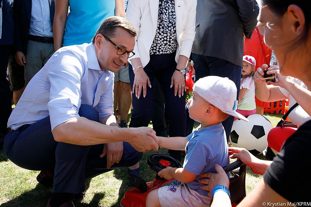 Uśmiechnięty premier Mateusz Morawiecki ściska dłoń małego chłopca.