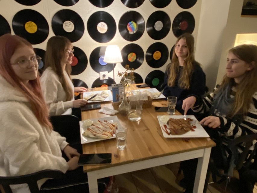 Zdjęcie kolorowe. Czworo uczniów przy stoliku. Jedzą naleśniki. W tle płyty gramofonowe.
