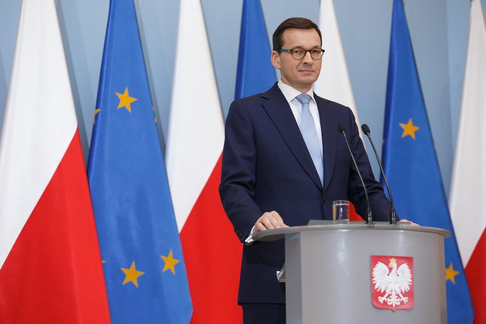 Premier Mateusz Morawiecki przy mówinicy, w tle flagi Polski i Unii Europejskiej.