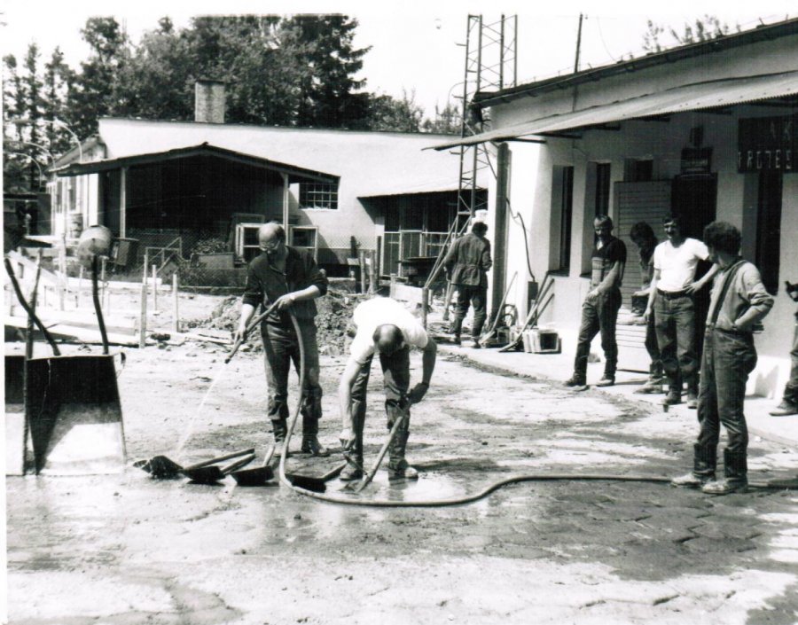 Na zdjęciu pracownicy ubrani w ubrania robocze czyszczą i myją narzędzia budowlane. W tle budynki magazynowe KP PSP Myślenice.