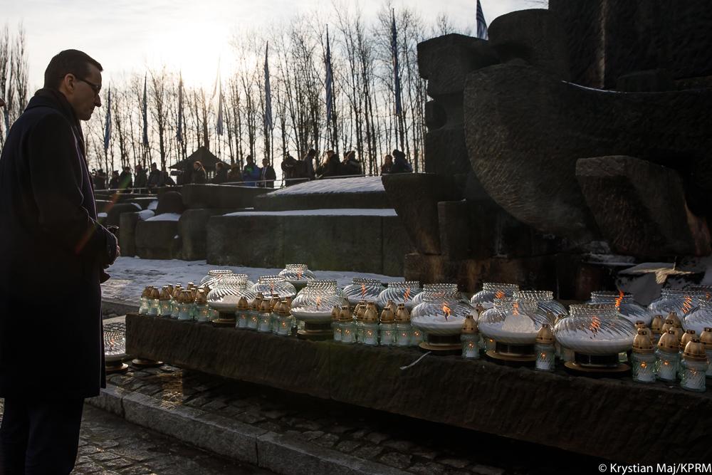 Premier Mateusz Morawiecki, a po prawo Pomnik Ofiar ze zniczami.