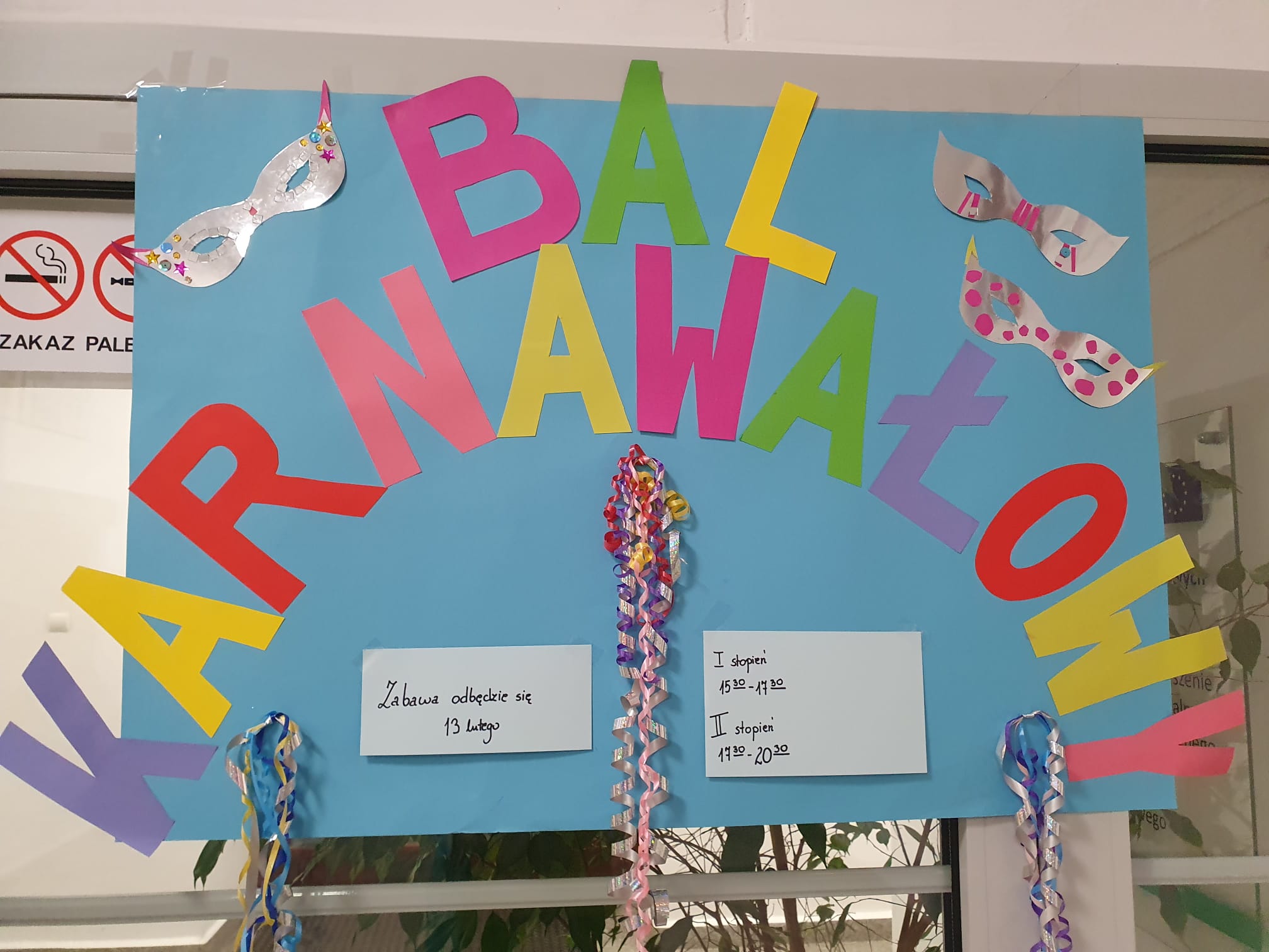 Plakat zdjęcie - Collage - wycinanka na niebieskim tle kolorowe litery i napis Bal Karnawałowy, srebrne maski na oczy, białe kartki doklejone do niebieskiego kartonu z odręcznymi napisami Zabawa odbędzie się 13 lutego, I stopień 15.30-17.30 oraz II stopnia 17.30-20.30, doczepione serpentyny. 