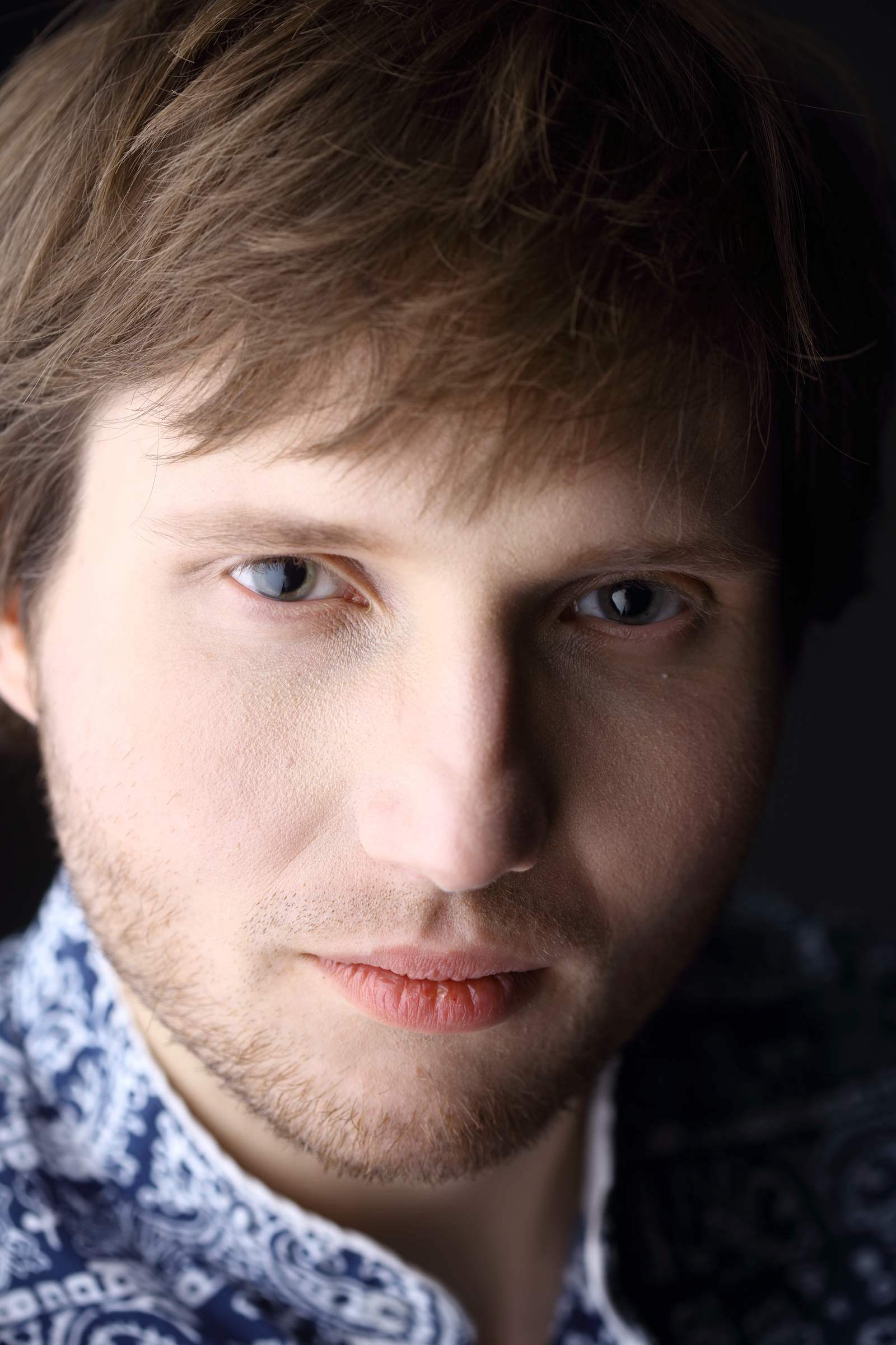 Zdjęcie przedstawiające twarz mężczyzny na ciemnym tle. 