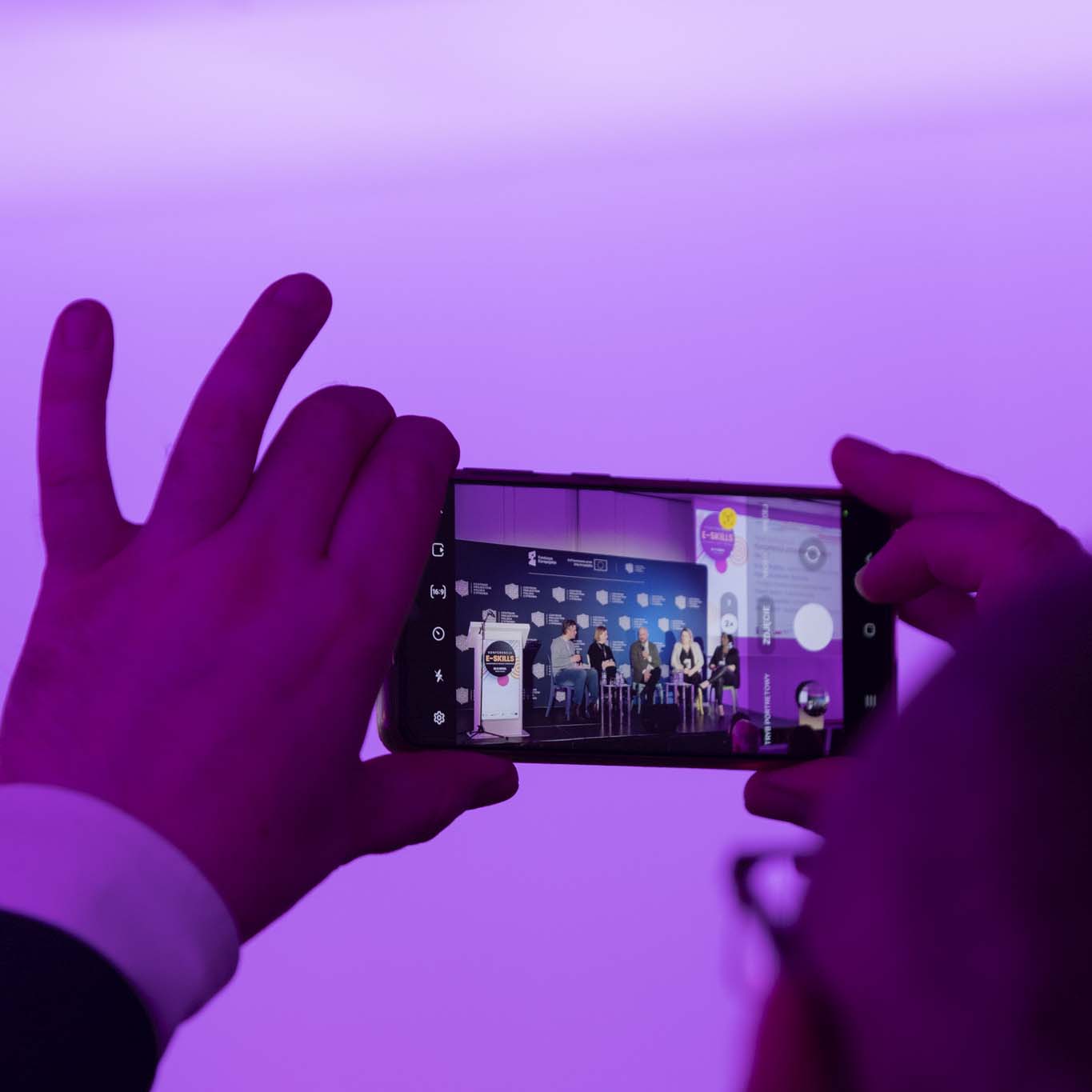 Ręce osoby trzymającej smartfon. Robi zdjęcie uczestnikom panelu.