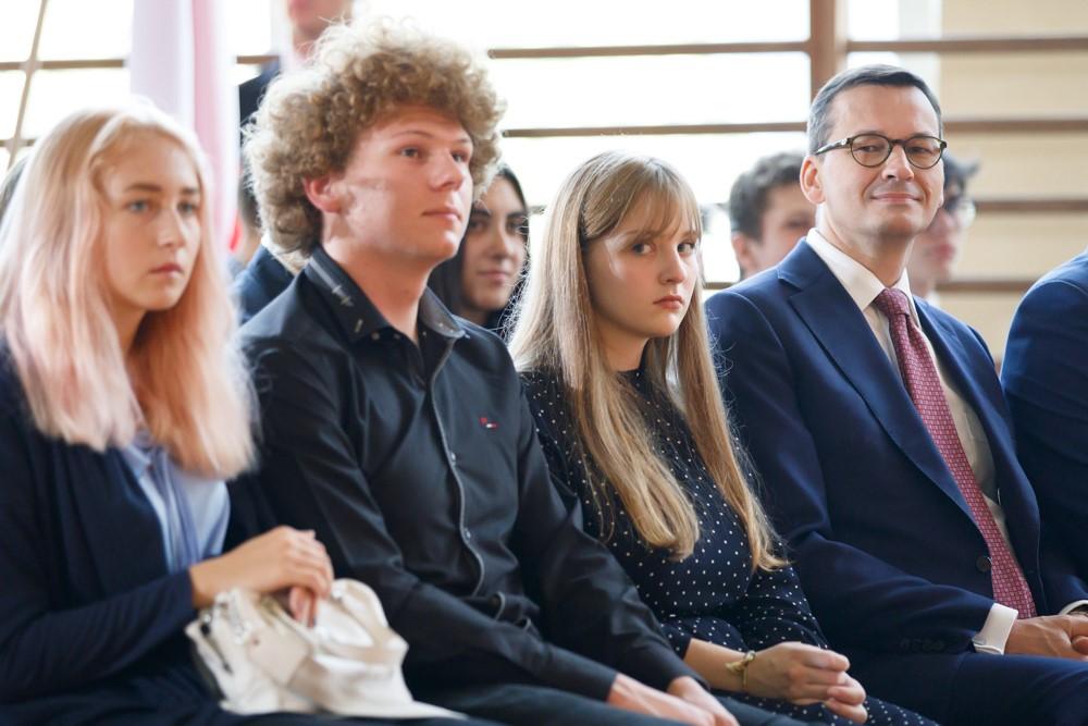 Premier Mateusz Morawiecki siedzi obok uczniów.