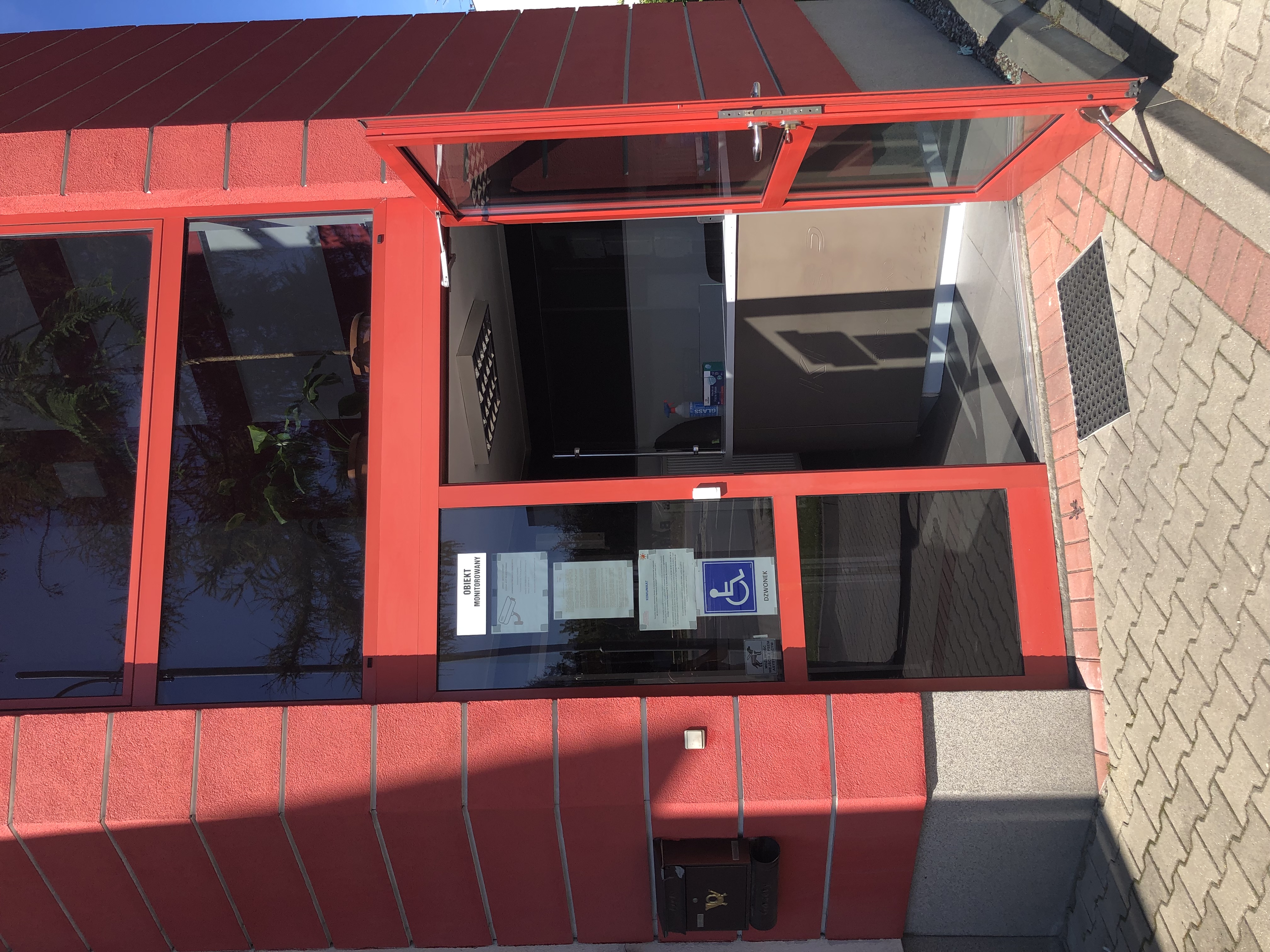 Otwarte drzwi do budynku komendy. Po lewej stronie drzwi przycisk dzwonka. W głębi widać biurko Podoficera dyżurnego.