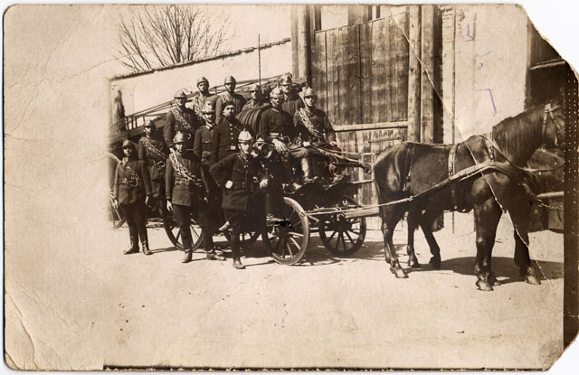 Zaprzęg konny Miejskiej Straży Pożarnej w Nowym Sączu stojący przed wspinalnią a obok niego strażacy w mundurach i z hełmami na głowach.