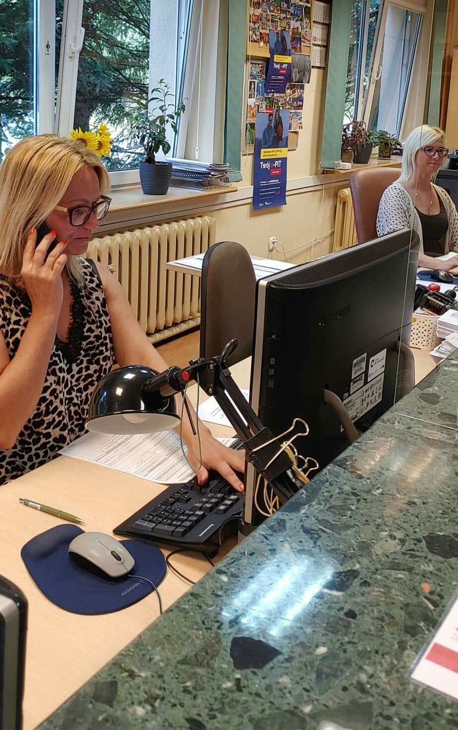 Wnętrze sali obsługi - przy biurkach siedzą dwie kobiety, jedna rozmawia przez telefon