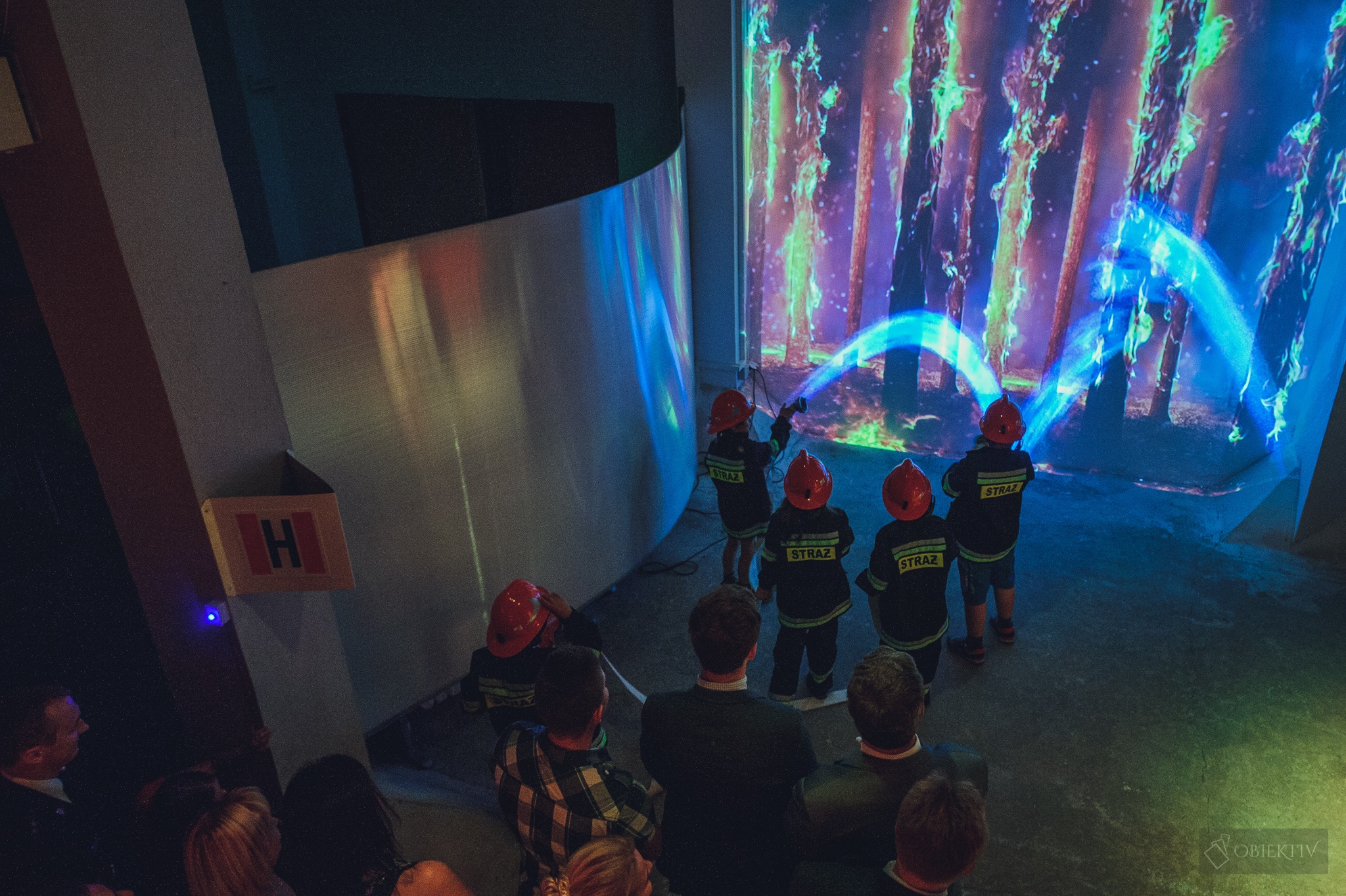 Zdjęcie przedstawia grupę dzieci ubranych w stroje strażackie, które za pomocą symulacji komputerowej uczą się gasić pożary