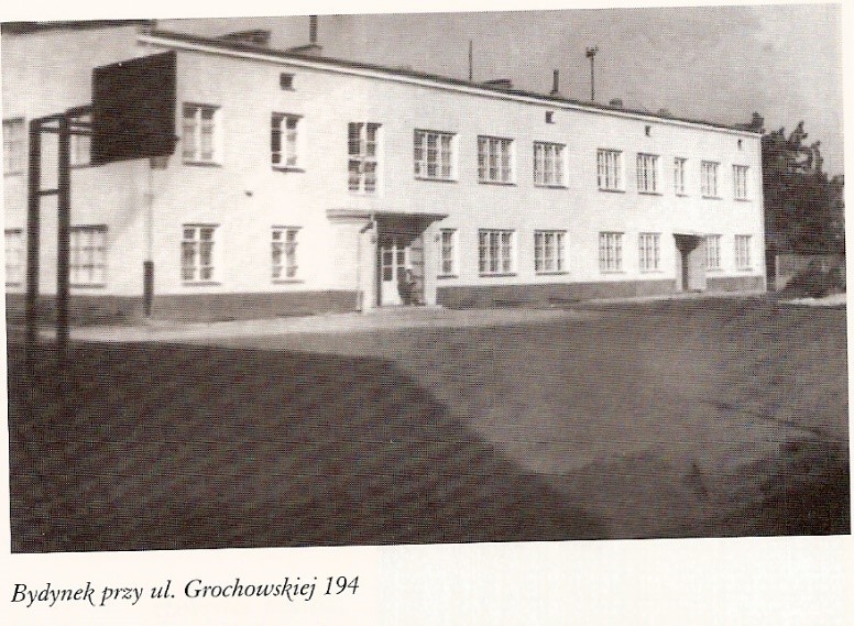 zdjęcie archiwalne, czarno-białe - jednopiętrowy budynek szkolny w jasnym kolorze, przed budynkiem boisko do koszykówki