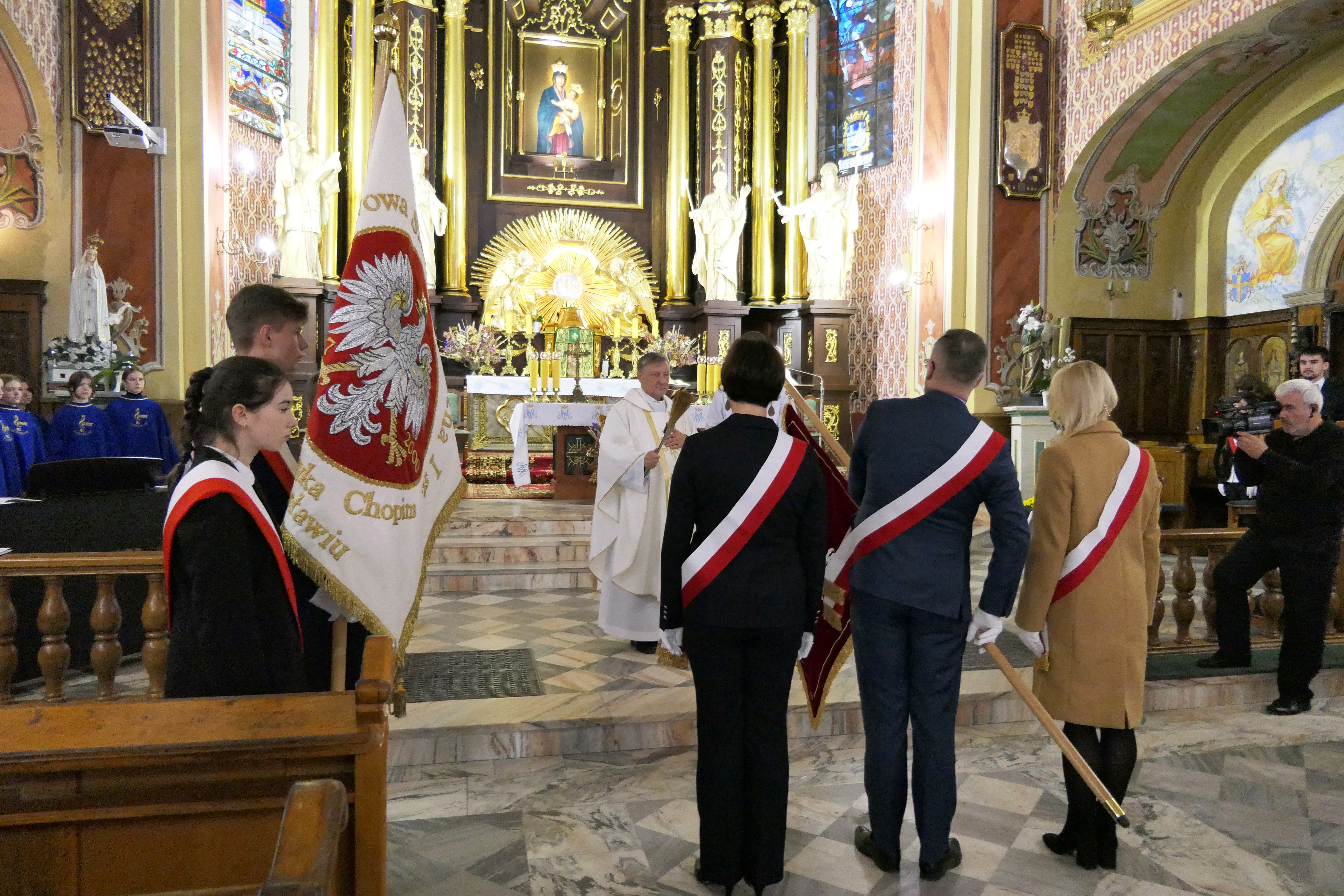 Zdjęcie z uroczystej Mszy św. w Kolegiacie pw. Bożego Ciała, podczas której Proboszcz Parafii ks. Prałat Marian Bocho poświęcił nowy sztandar ZPSM im. F. Chopina w Jarosławiu. Po lewej stronie w oddali uczniowie Chóru PSM I st., dalej poczet sztandarowy uczniów PSM I st. ze sztandarem szkoły, dalej Proboszcz Parafii ks. Prałat Marian Bocho, dalej Rada Rodziców ZPSM im. F. Chopina w Jarosławiu ze sztandarem.