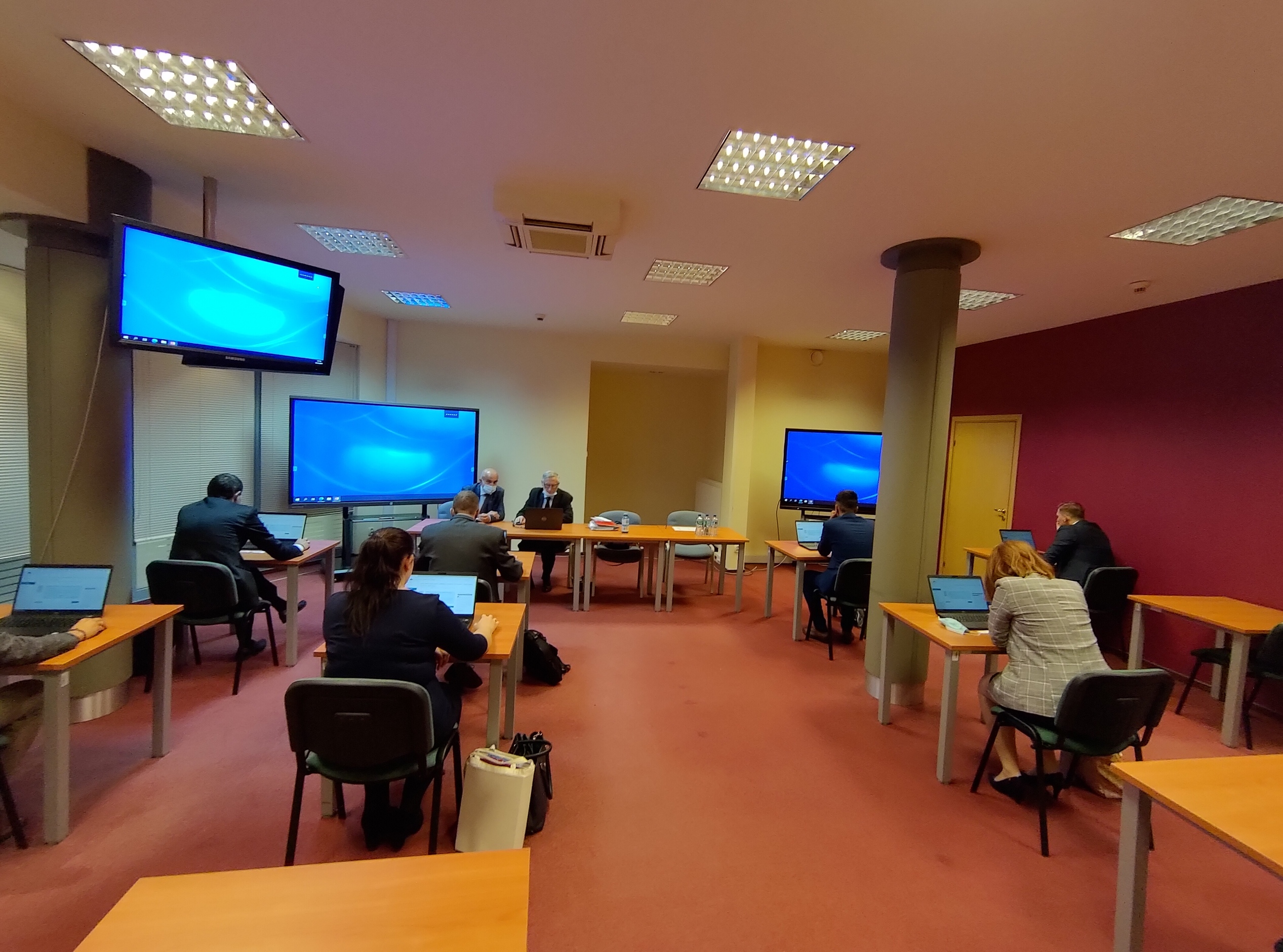 Zdjęcie przedstawia salę egzaminacyjną z z członkami Komisji egzaminacyjnej i osobami przystępującymi do egzaminu siedzącymi pojedynczo przed laptopami.