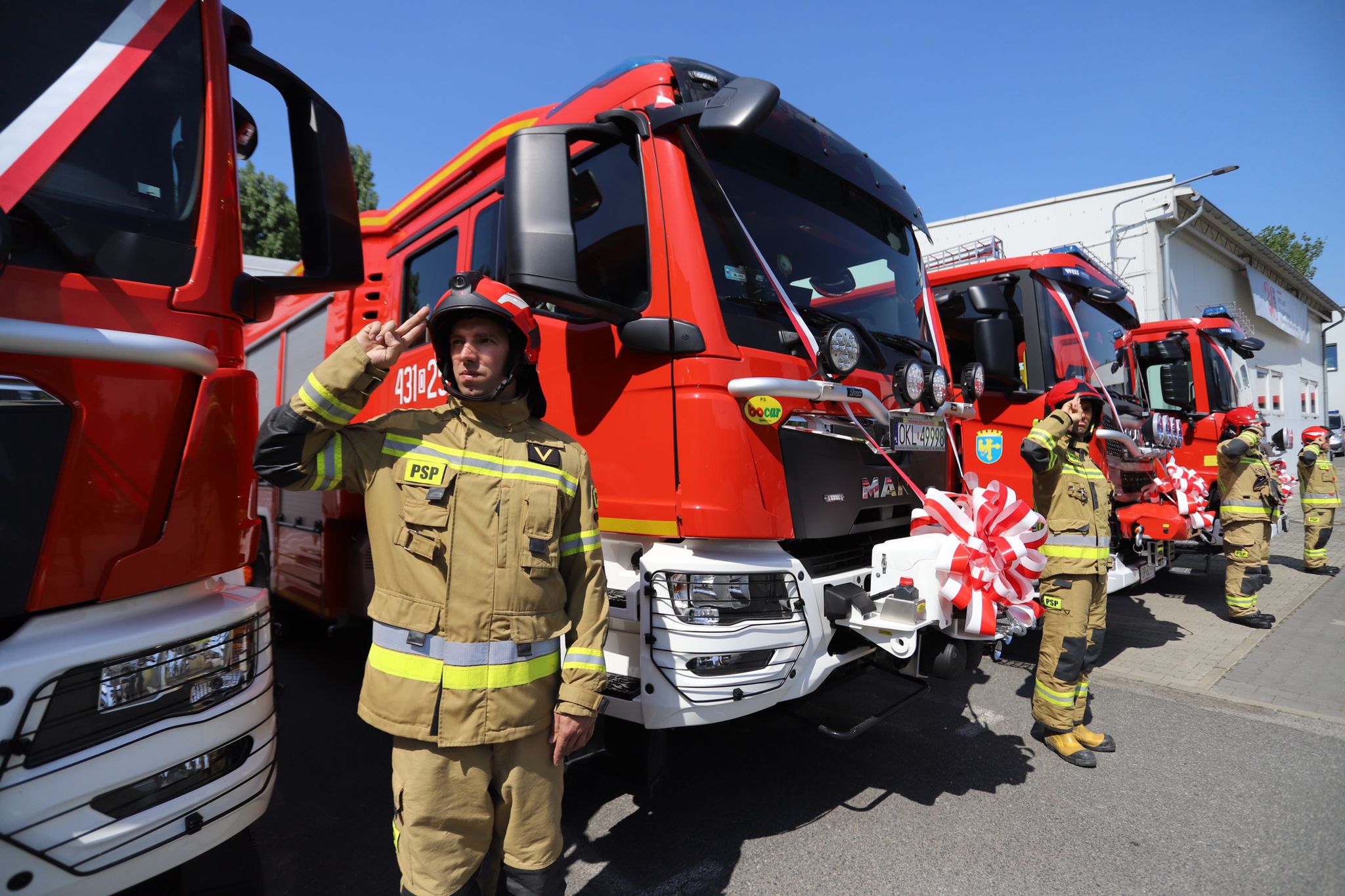 Na zdjęciu widać strażaków PSP w ubraniu bojowym stojących na tle przekazanych samochodów. 