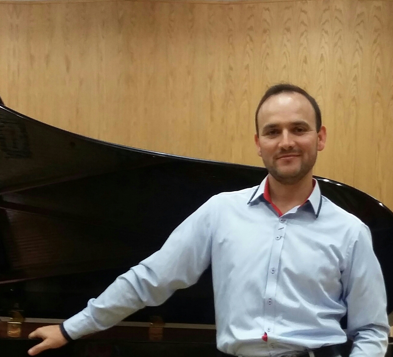 zdjęcie przedstawiające Pawła Pecuszok - tenor. Na zdjęciu artysta w jasnej koszuli oparty o fortepian.
