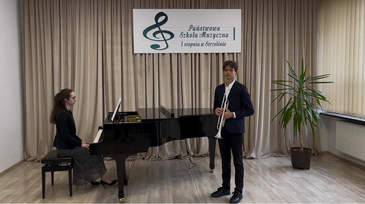Na zdjęciu widoczny jest stojący uczeń z trąbką i akompaniator siedzący przy fortepianie