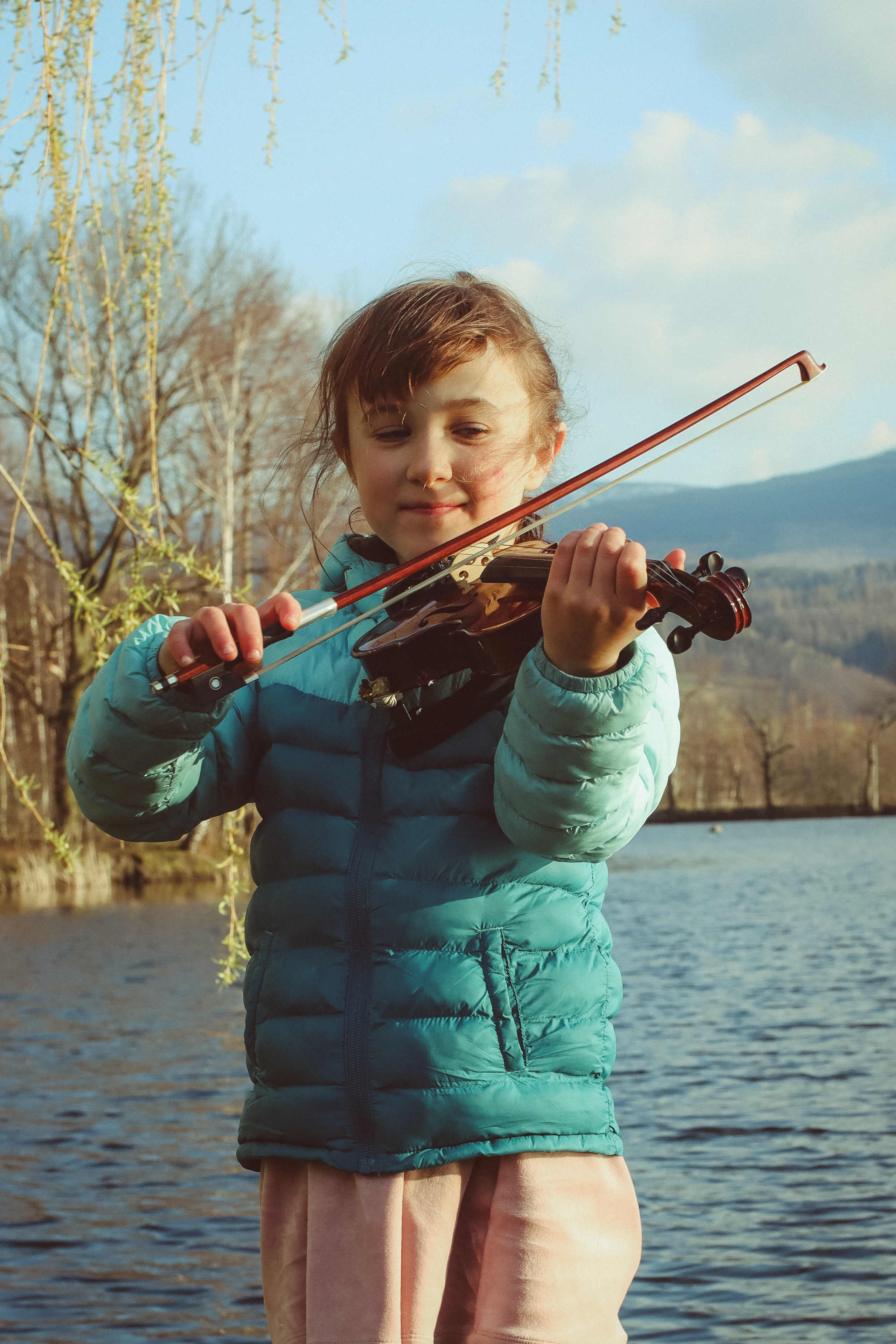 Zdjęcie postaci dziewczynki: Ronji Wójtowicz-Stambulskiej zrobione na potrzeby konkursu. W tle jezioro, dziewczynka trzyma altówkę, w pozycji sugerującej granie na instrumencie