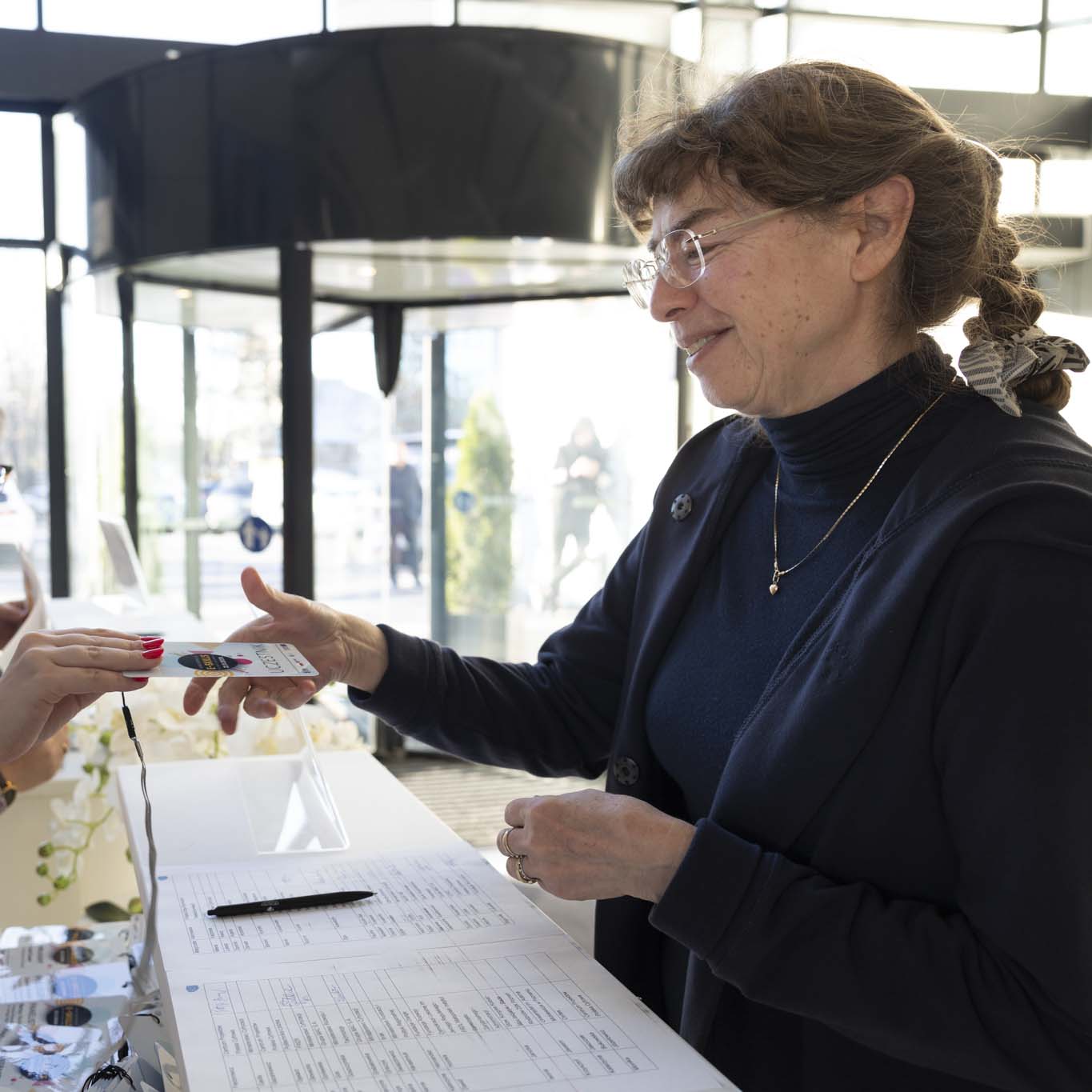Kobieta odbiera plakietkę uczestnika konferencji. Uśmiecha się.