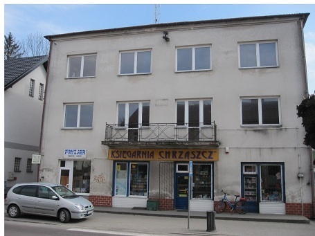 Zdjęcie przedstawia jasny budynek z dużą ilością okien. Na dole budynku ceglany cokół. Na parterze widoczne wejście do księgarni chrząszcz. 