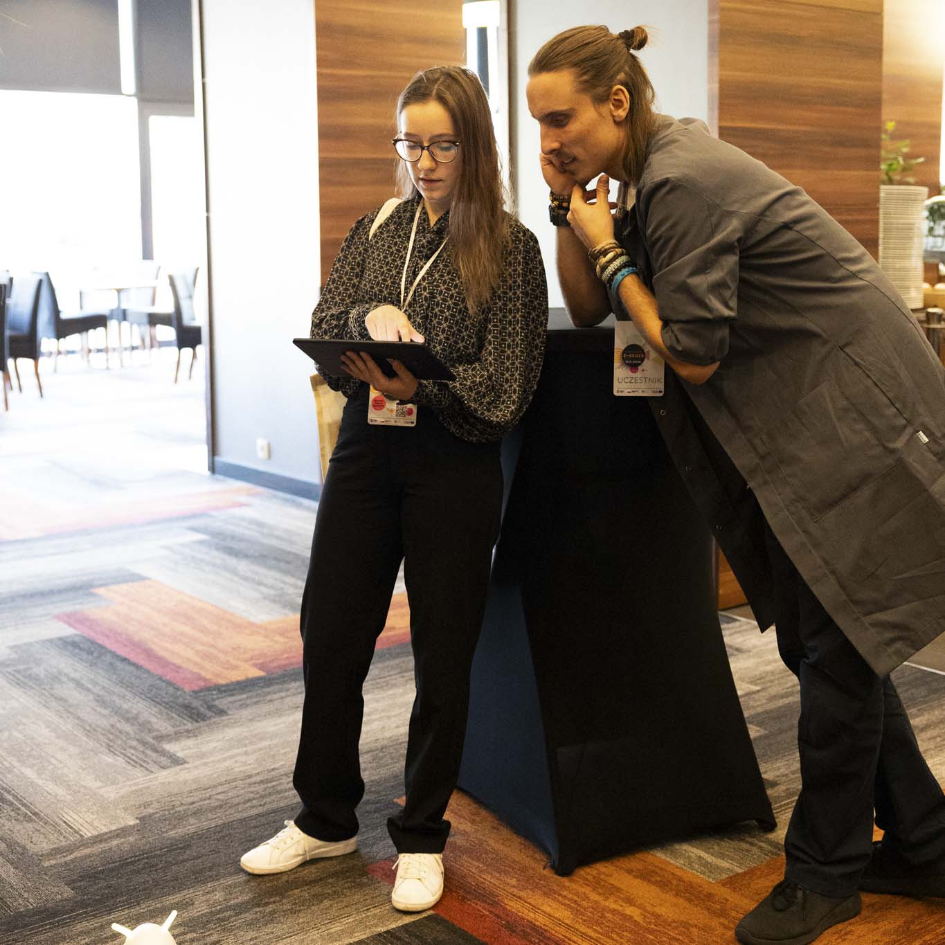 Pani Antonina Nagler trzyma w rękach tablet. Obok stoi mężczyzna z Centrum Nauki Kopernik i obserwuje ekran tabletu.