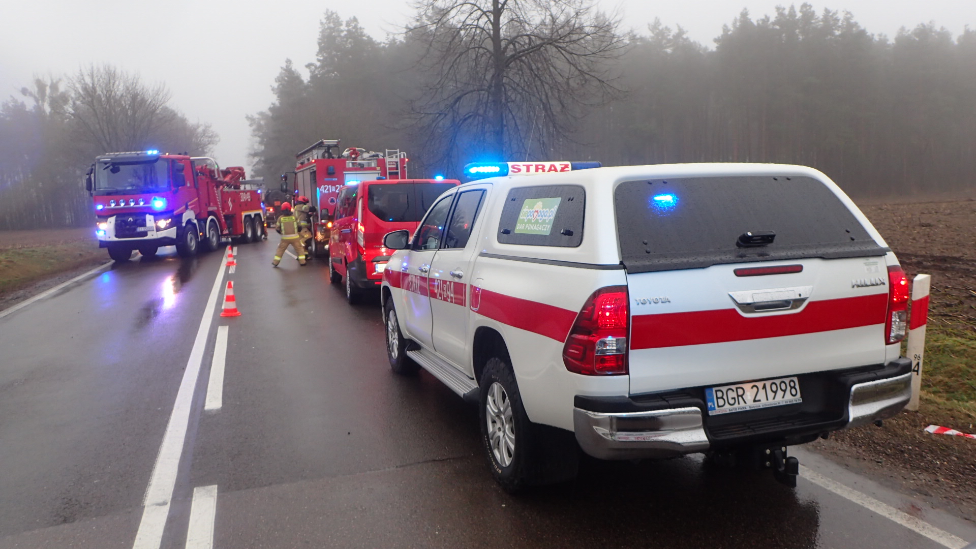 Pojazdy ratownicze straży pożarnej stoją na drodze z włączonymi światłami ostrzegawczymi.