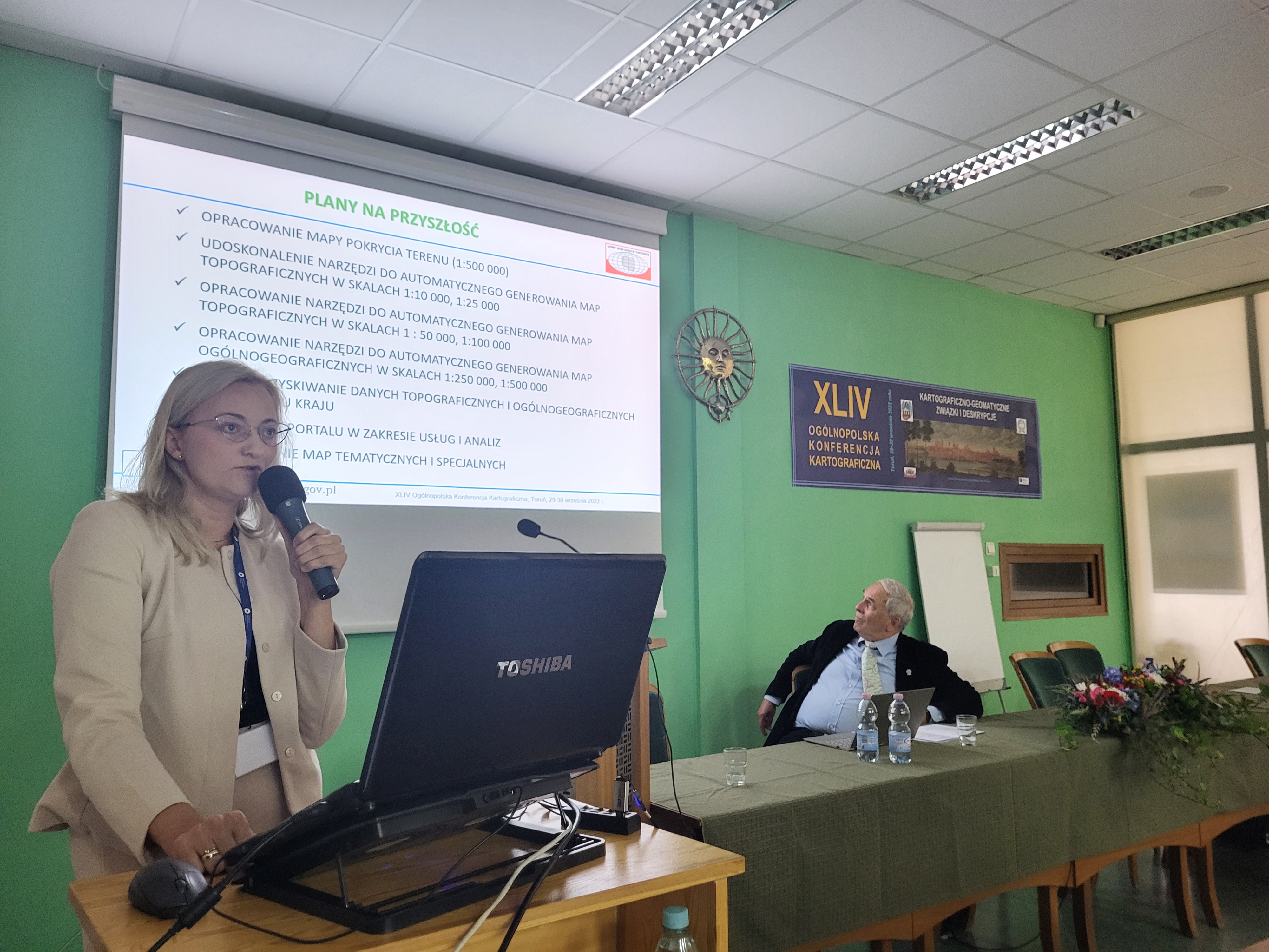 Zdjęcie przedstawia Annę Bober, Dyrektor Departamentu Geodezji, Kartografii i Systemów Informacji Geograficznej w trakcie wygłaszanego w imieniu p.o. GGK referatu dot. działań GGK w obszarze kartografii