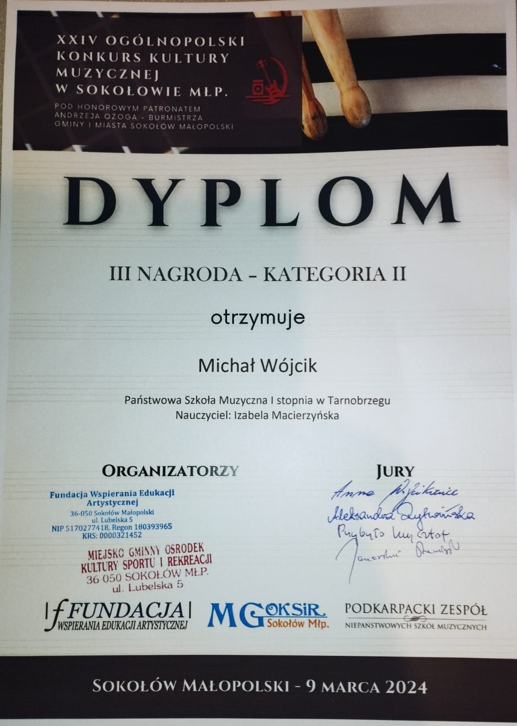Dyplom za otrzymanie III Nagrody. Na górze ilustracja przedstawiająca pałeczki perkusyjne. Na dole po prawej stronie podpisy Jury, a po lewej stronie podpisy organizatorów.