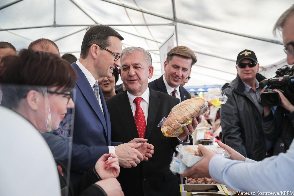 Premier Mateusz Morawiecki patrzy na chleb, wokół niego ludzie.