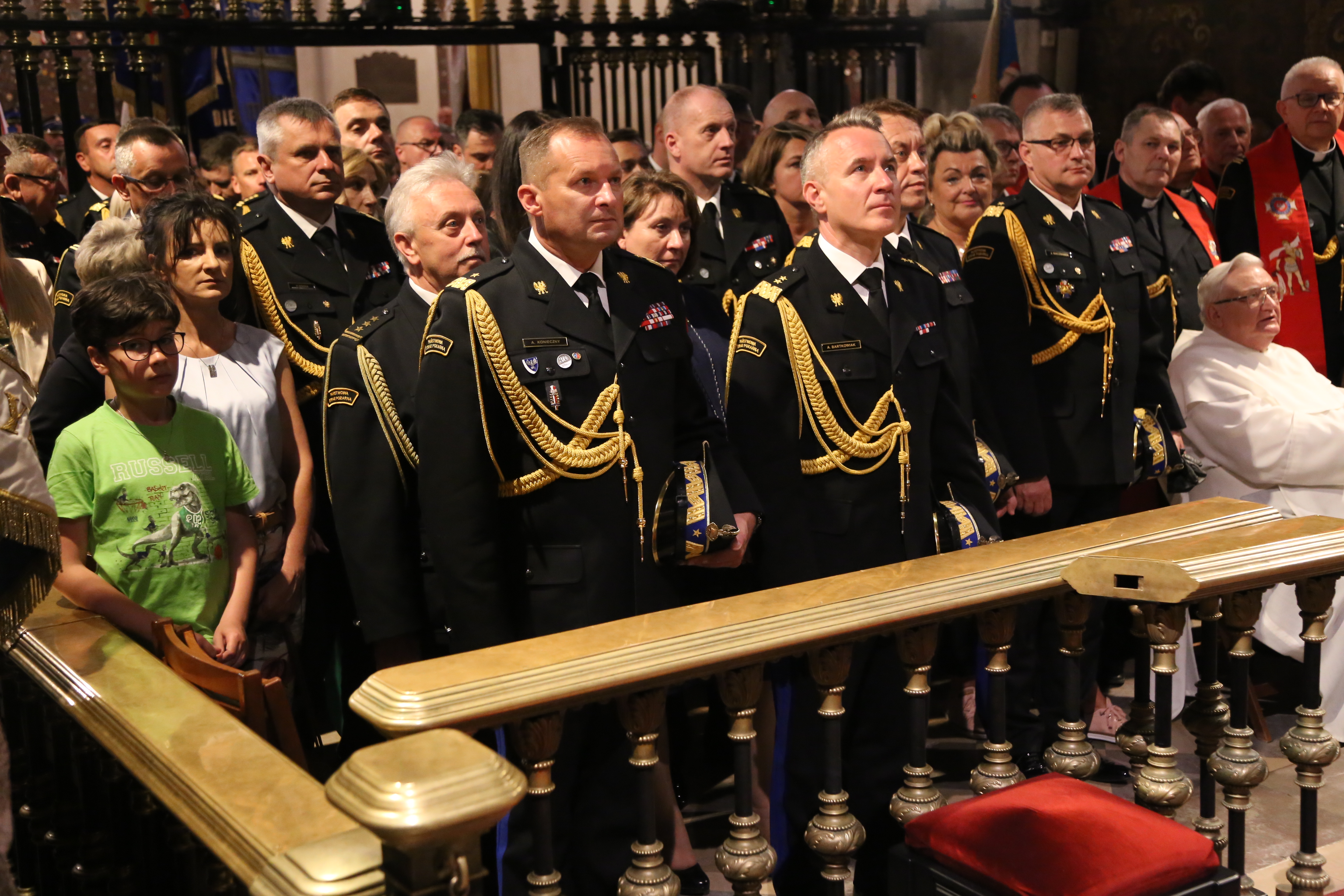 W ławach kościelnych stoją strażacy oraz osoby cywilne , modląc się w Apelu Jasnogórskim
