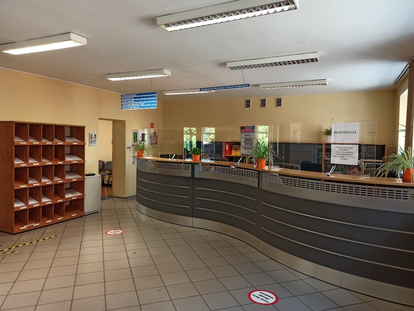 Wnętrze sali obsługi - wysoka lada, obok regał na ulotki