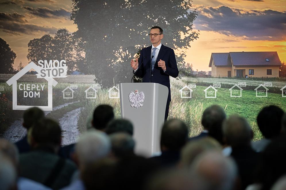Premier Mateusz Morawiecki przemawia na mównicy na tle napisu "Smog stop","Ciepły Dom".