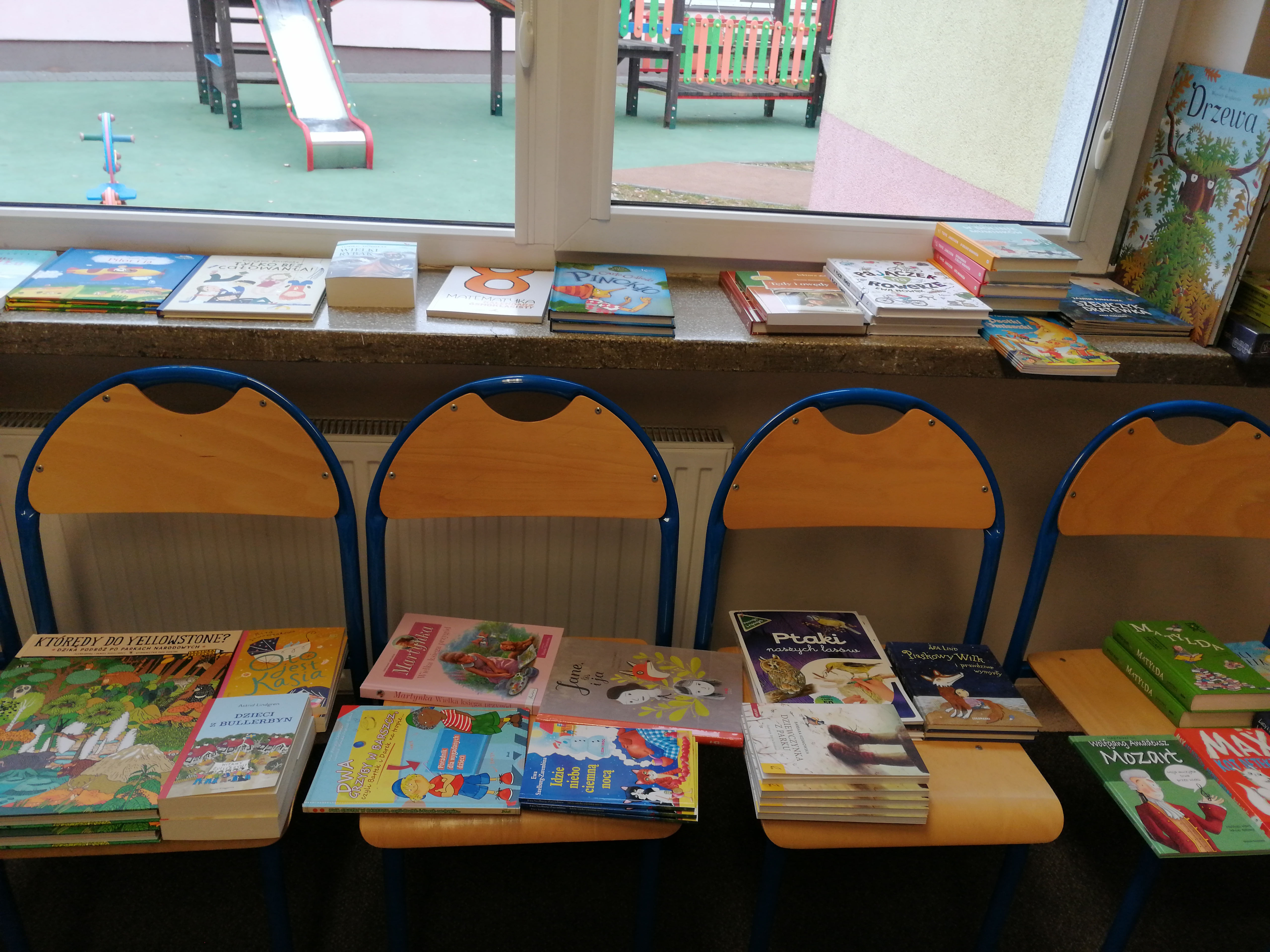 Książki dla dzieci z programu rozwoju czytelnictwa rozłożone na czterech krzesełkach szkolnych
