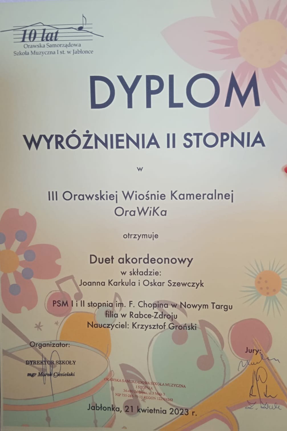 Dyplom w pastelowych kolorach. W lewym górnym rogu logo organizatora konkursu, z prawej strony kolorowy pastelowy kwiat. Od góry pośrodku pełna nazwa imprezy, oraz skład duetu i nazwa szkoły oraz dane nauczyciela. Na dole miejsce i data konkursu. W dolnej części dyplomu kolorowe kwiaty, nutki, bębenek oraz trąbka.