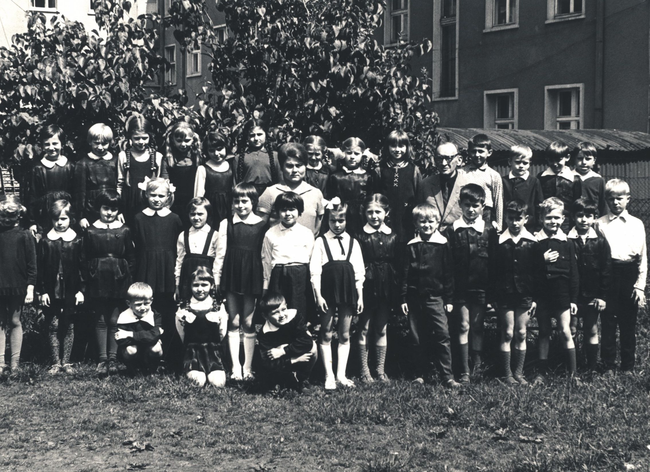 Zdjęcie przedstawia dużą grupę uczniów szkoły. Pomiędzy nimi w środku stoją pani Wanda Babiej oraz dyrektor Tadeusz Rękas. Dzieci stoją w dwóch rzędach, troje siedzi na trawie przed pozostałymi. W tle drzewa i zabudowania mieszkalne,