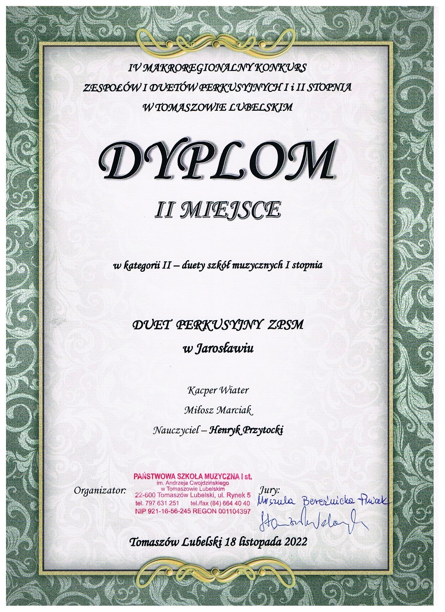 Dyplom na szarym tle z ozdobnym obramowaniem w kolorach metalicznym i szaroniebieskim. Od góry następujące napisy: IV Makroregionalny Konkurs Zespołów i Duetów Instrumentów Perkusyjnych I i II st. w Tomaszowie Lubelskim. Poniżej dużą czcionką napis DYPLOM II MIEJSCE poniżej w kategorii II - duety szkół muzycznych I stopnia. Poniżej napis: DUET PERKUSYJNY ZPSM w Jarosławiu. Kacper Wiater, Miłosz Marciak, Nauczyciel - Henryk Przytocki. Poniżej napis organizator i pieczęć: Kontakt Państwowa Szkoła Muzyczna I st. im. Andrzeja Cwojdzińskiego w Tomaszowie Lubelskim 22-600 Tomaszów Lubelski, ul. Rynek 5 obok napis Jury i podpisy: Urszula Bereźnicka-Pniak, Stanisław Welanyk. Poniżej napis: Tomaszów Lubelski 18 listopada 2022