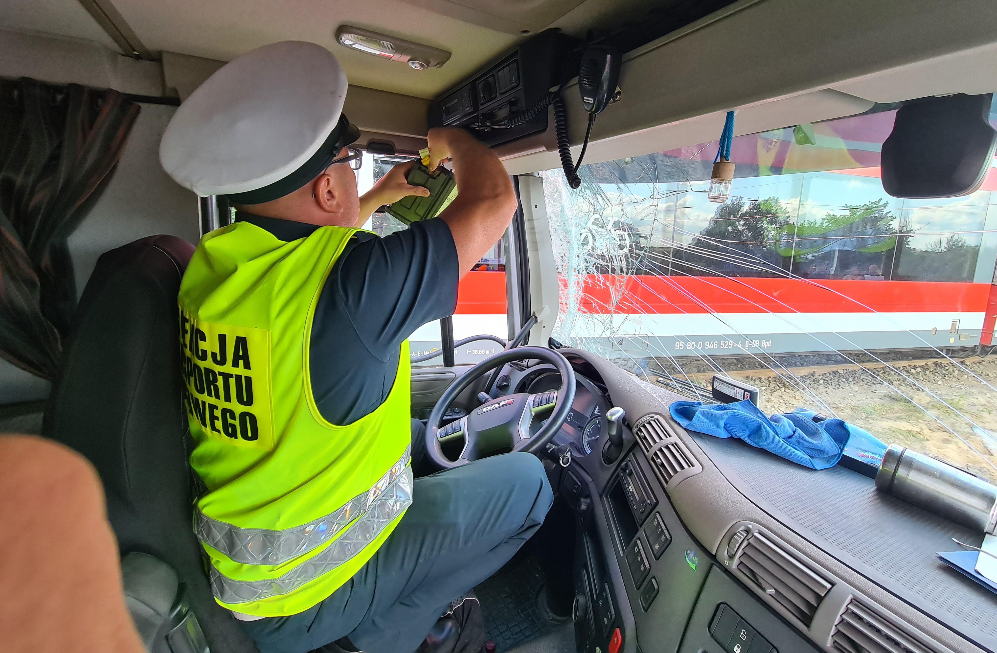 Inspektor siedzi na fotelu kierowcy ciężarówki i pobiera dane z tachografu cyfrowego.