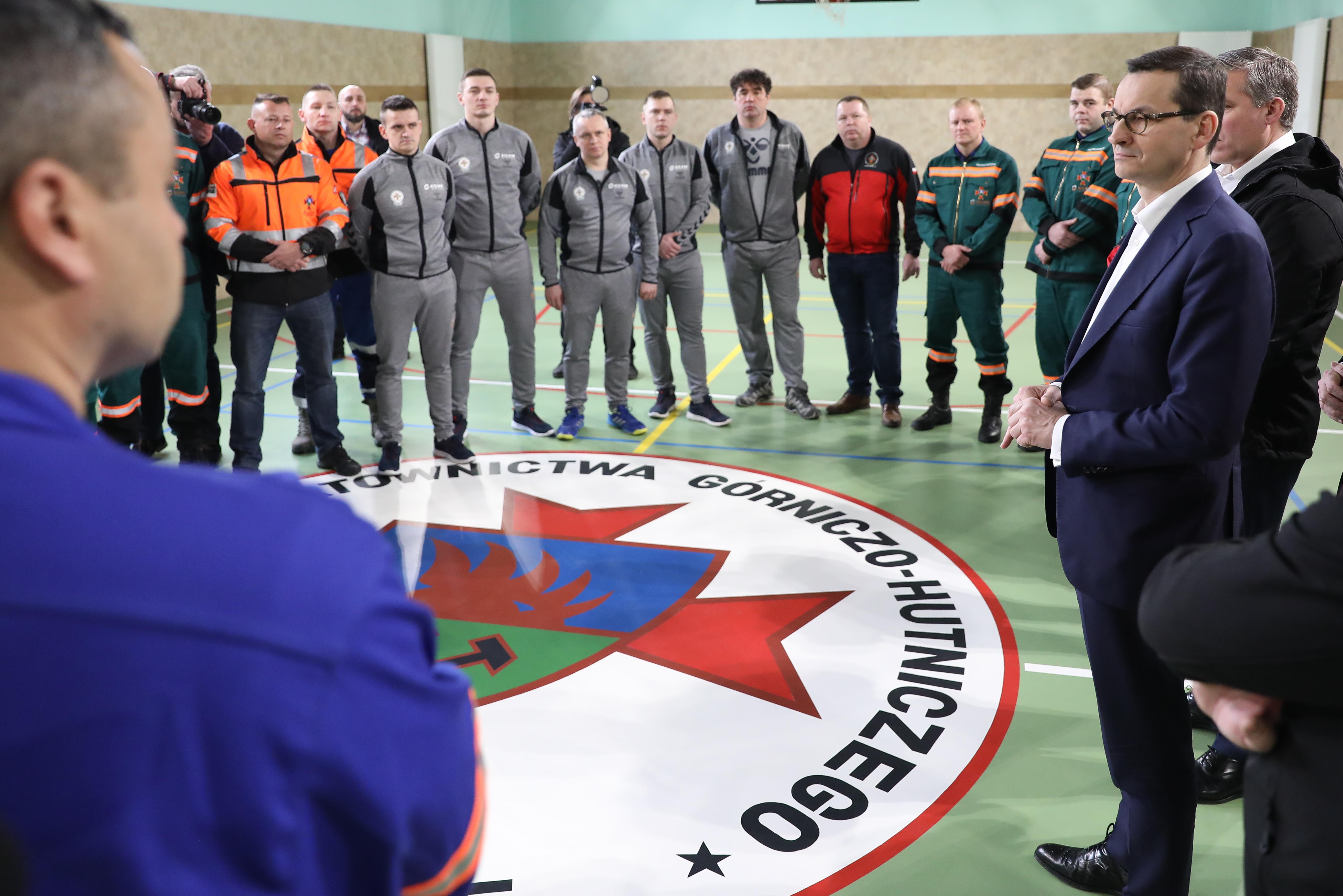 Premier Mateusz Morawiecki stoi z zespołem ratowniczym na sali gimnastycznej.