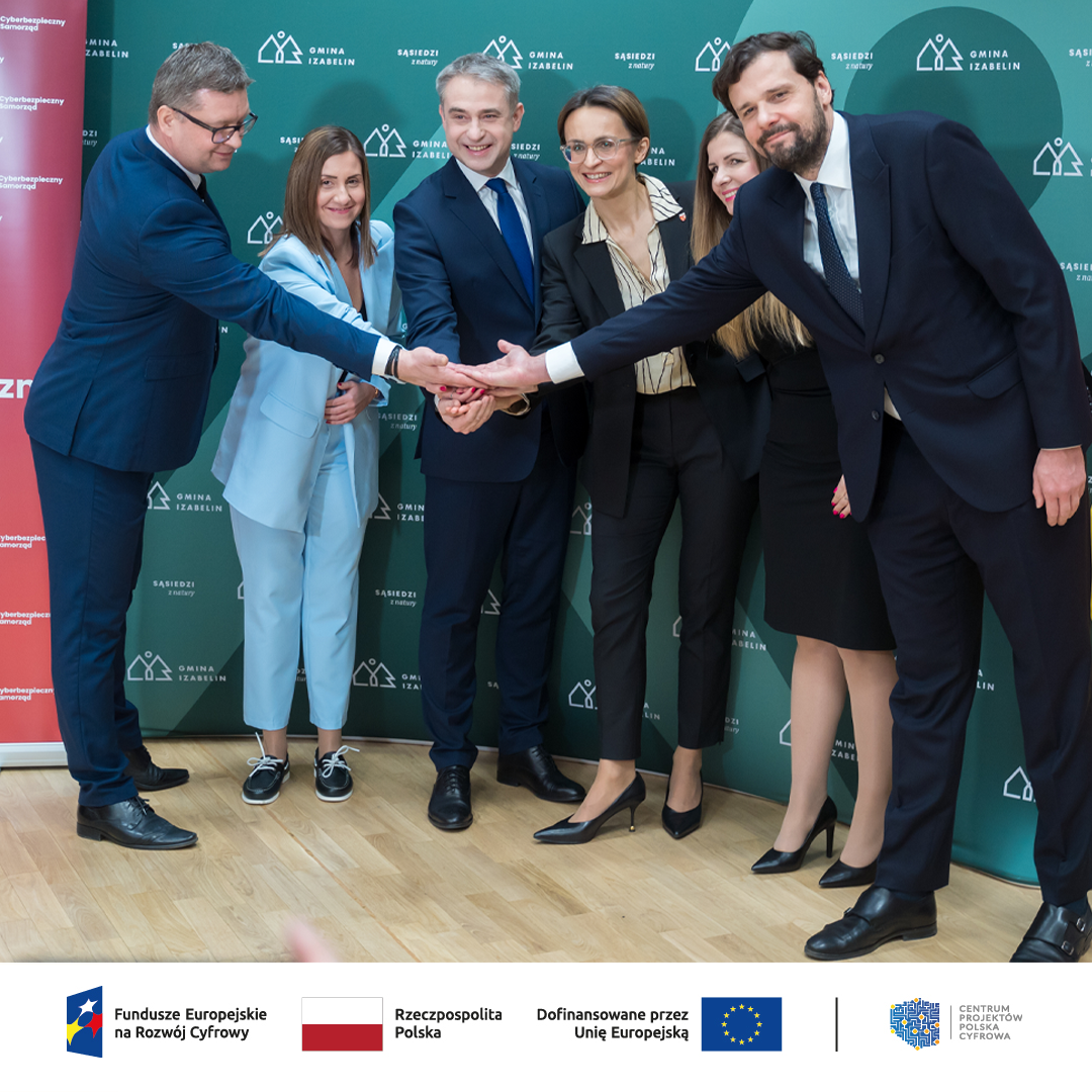 Od lewej Juliusz Brzostek, Maja Wolnik, Krzysztof Gawkowski, Dorota Zmarzlak , Agnieszka Woźniak oraz Wojciech Szajnar na tle ścianki gmina Izabelin podający sobie ręce