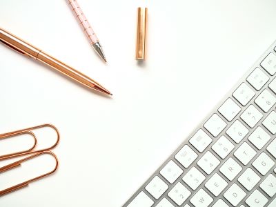 zdjęcie przedstawiające białą klawiaturę dwa złote spinacze oraz długopisy - grafika ozdobna