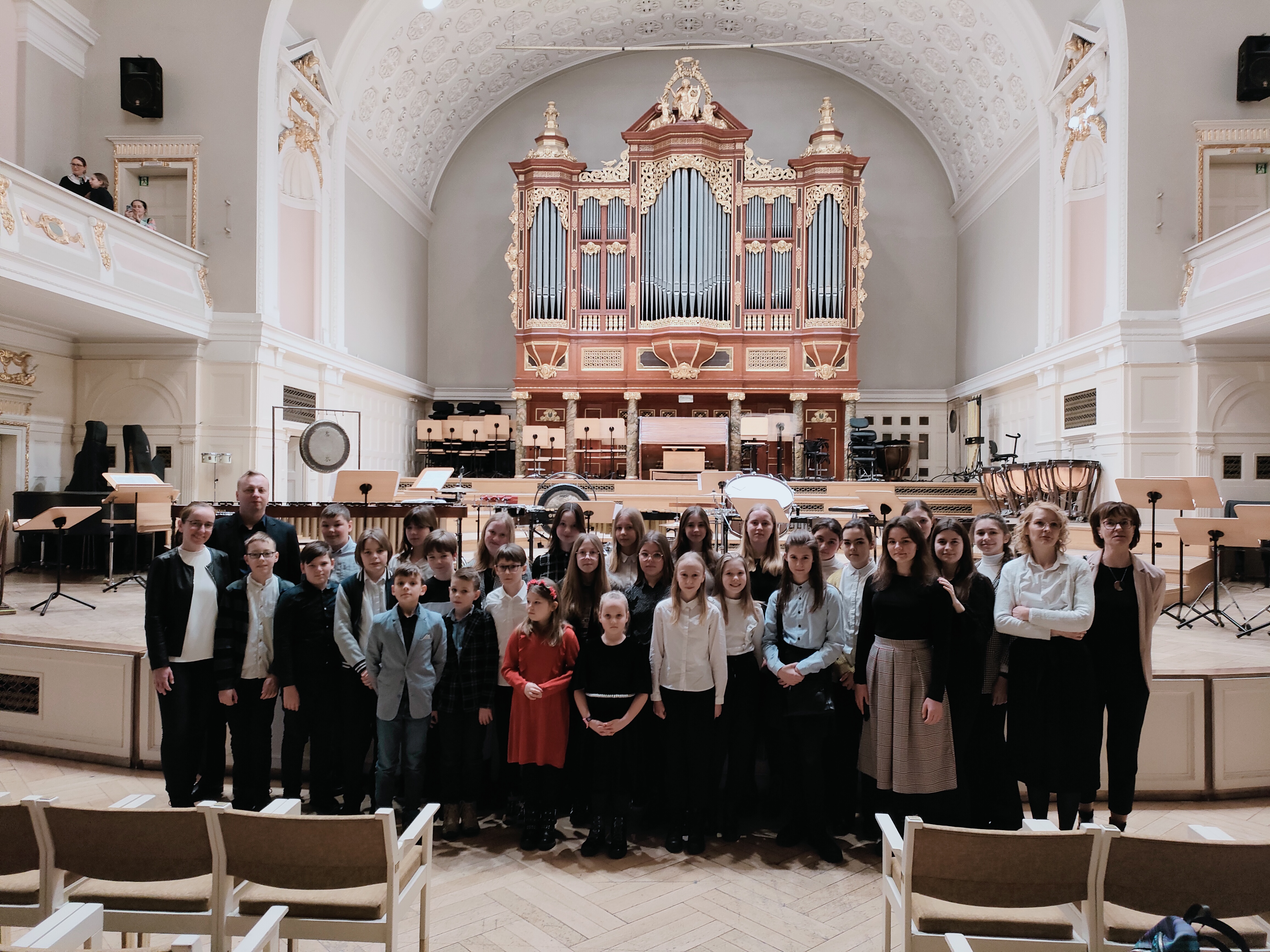 Zdjęcie przedstawia uczniów naszej szkoły stojących przed scenę w auli filharmonii poznańskiej. Na scenie stoja instrumenty perkusyjne oraz pulpity. W tle organy filharmonii. 