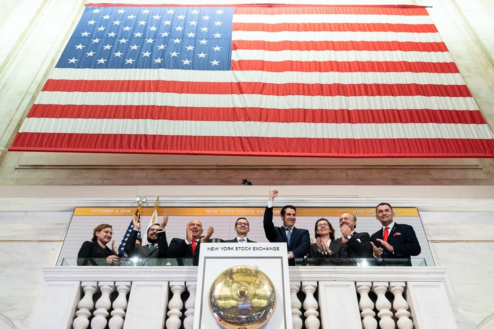 Premier Mateusz Morawiecki otwiera sesję giełdy, w tle flaga Stanów Zjednoczonych.