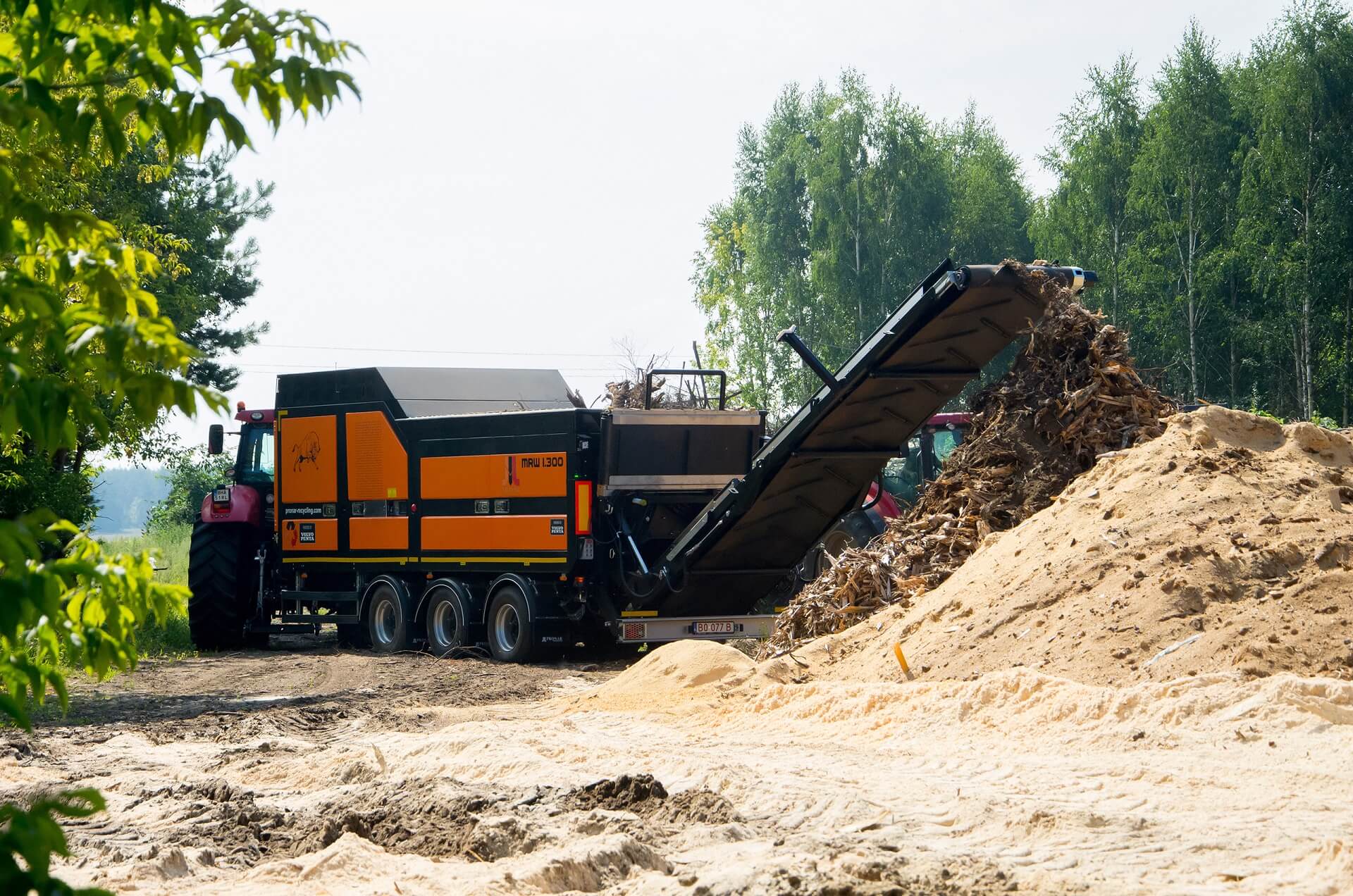 Mobile slow-speed shredder MRW 1.300. An orange machine the size of a combine works in the field, chopping wood