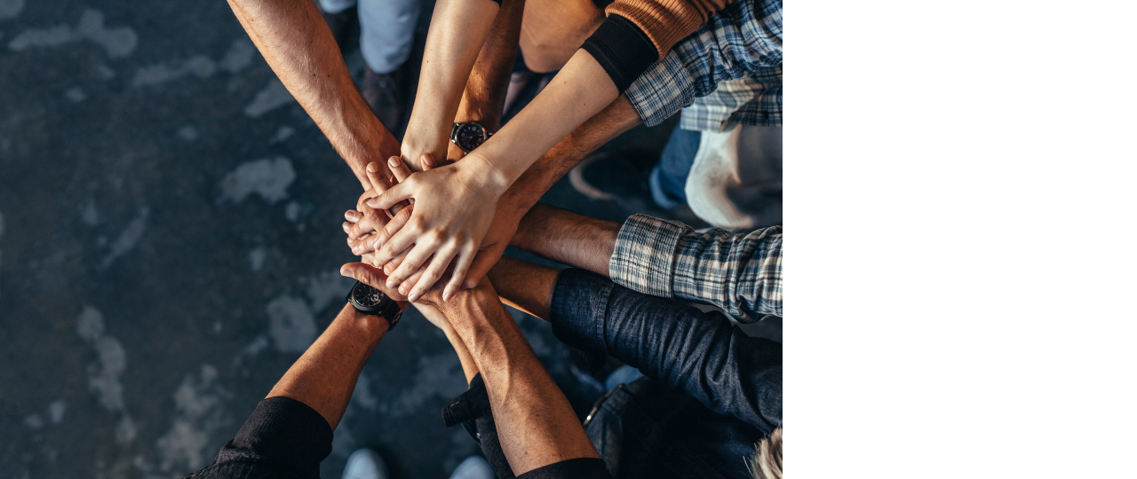 Widok z góry 10 rąk od łokcia do dłoni ułożone jedna na drugiej symbolizujących solidarność i wspólność. 