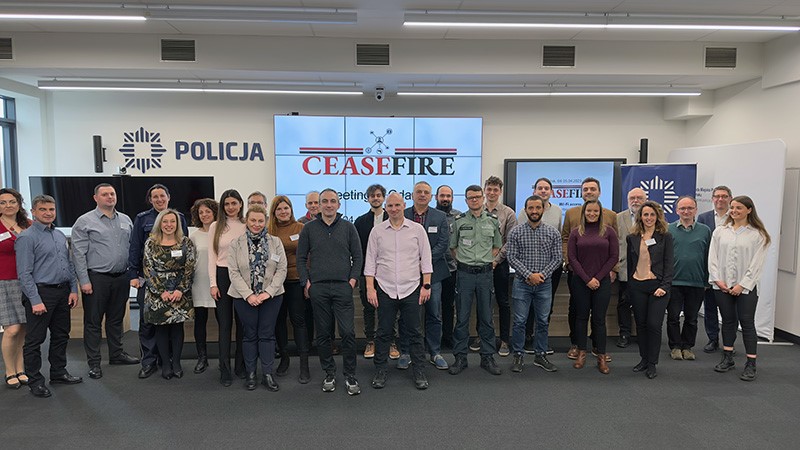 Grupa ludzi w pomieszczeniu, za nimi wyświetla się logo CEASEFIRE.