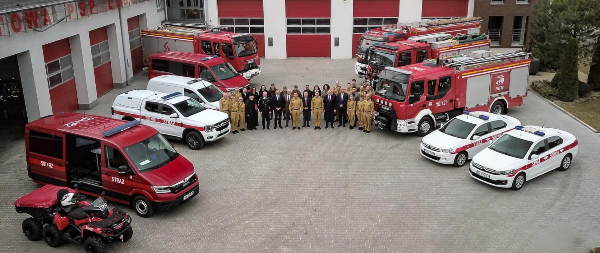 Na zdjęciu widać pojazdy KP PSP w Lublińcu przed garażami JRG, w środku grupa strażaków oraz zaproszonych gości pozuje do zdjęcia