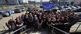 Grupa ludzi w granatowych koszulkach stoi przed schodami na dworze
