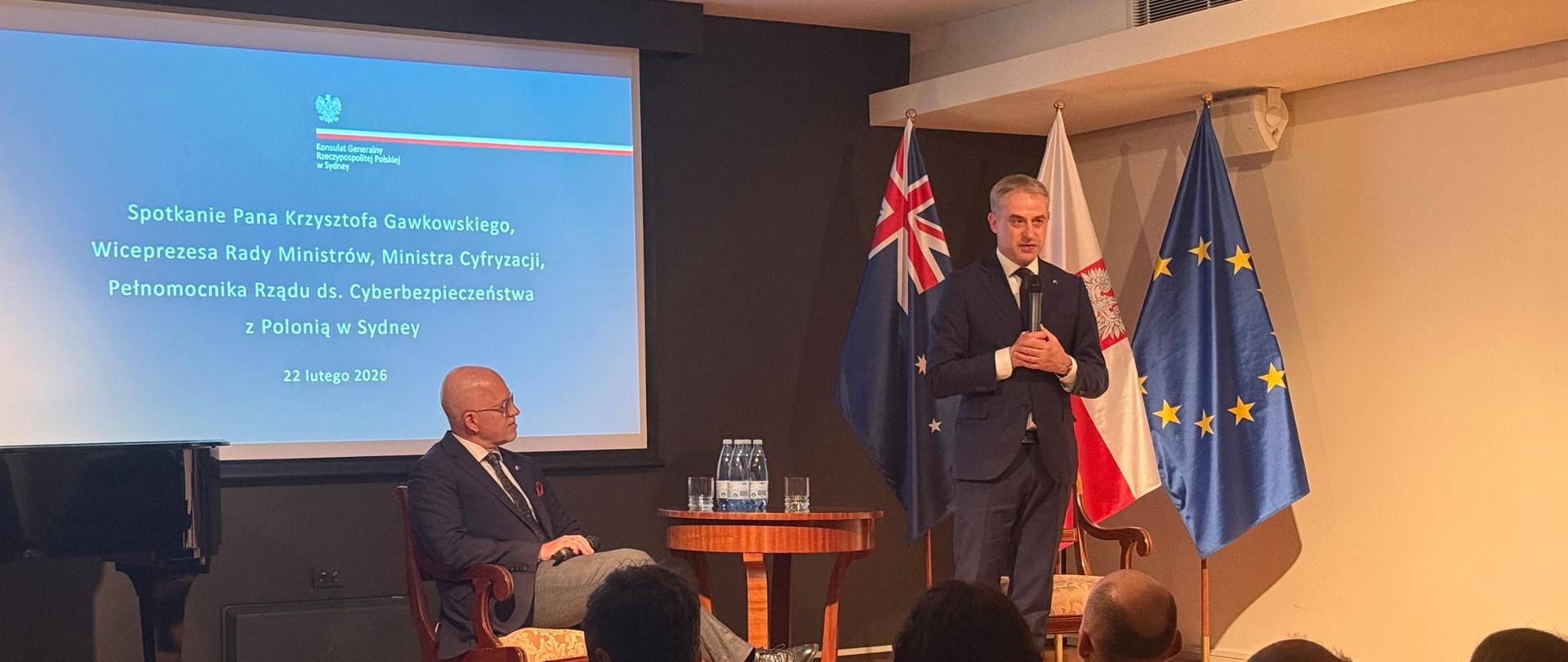 The photo shows two men in suits with microphones in their hands, with flags in the background.